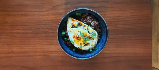 A bowl of congee topped with an egg, green onion, sesame seeds, and chili oil