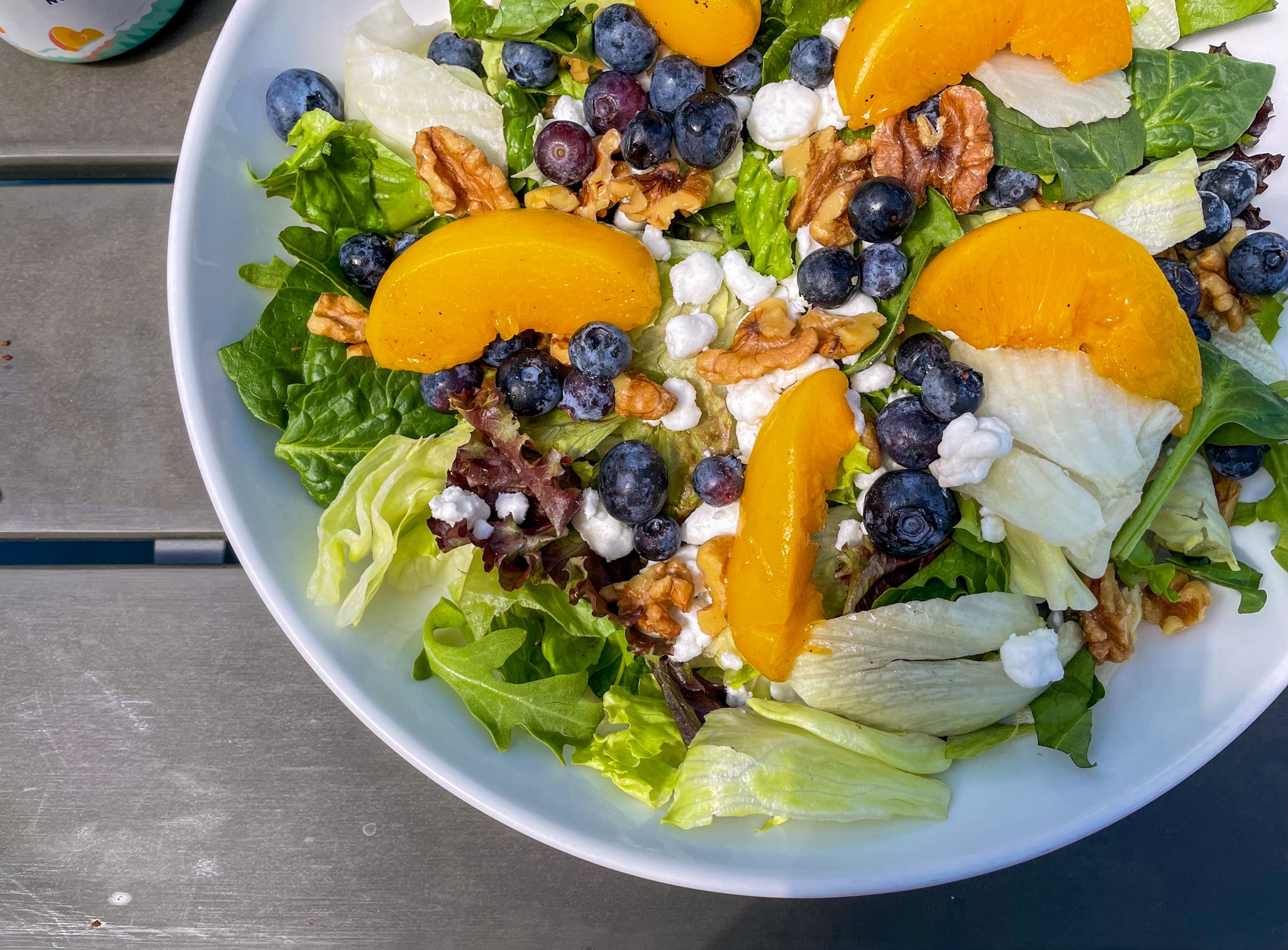 a big salad in a bowl with peaches, blueberries, and pecans