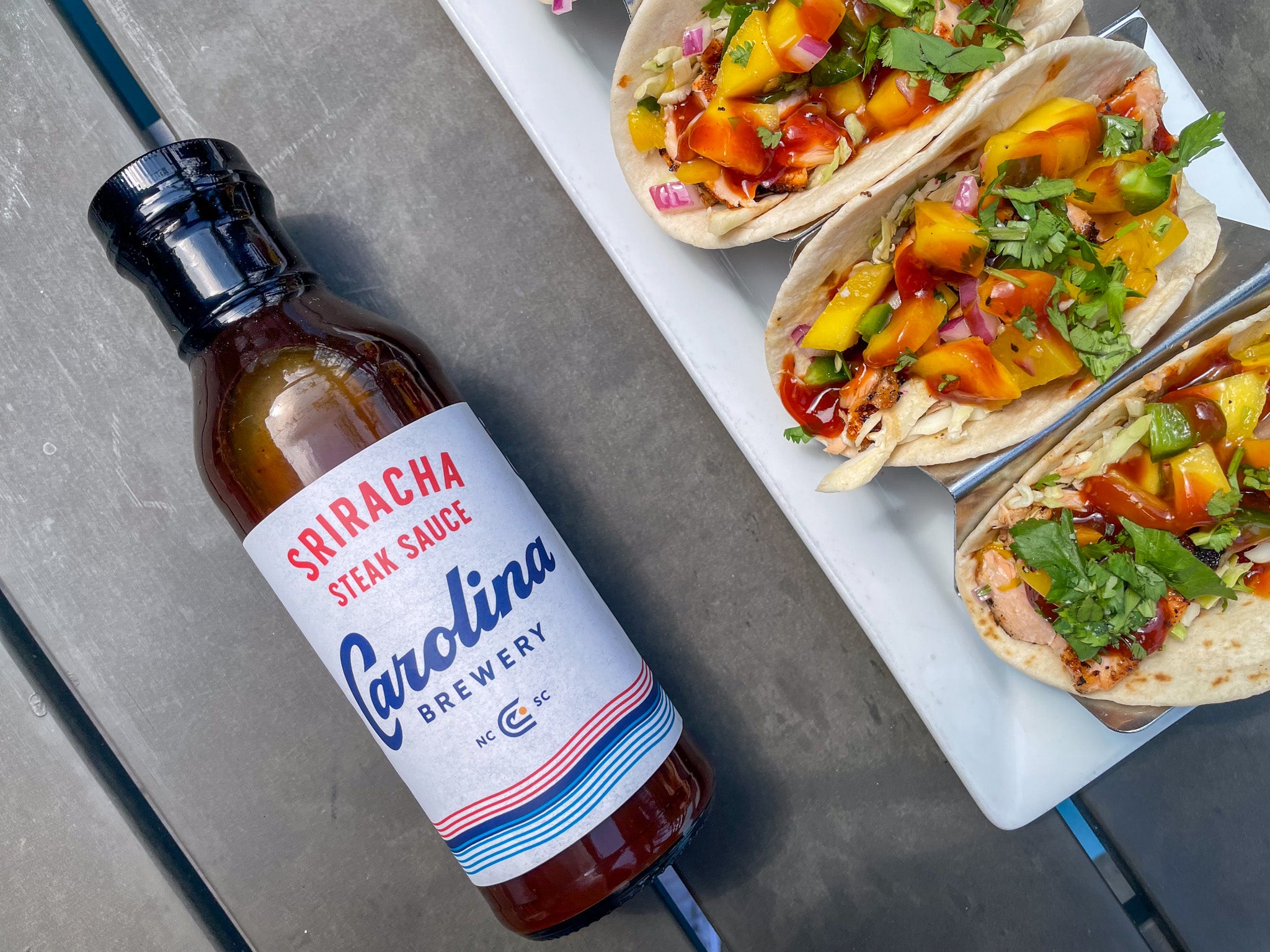 salmon tacos next to a bottle of Carolina Brewery's sriracha hot sauce