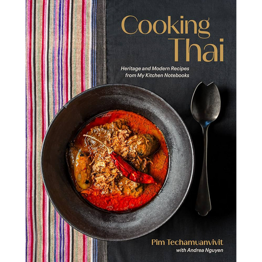 Book cover for 'Cooking Thai' by Pim Techamunivit with Andree Nguyen, featuring a bowl of red Thai curry with a dried red chili and a spoon on a dark background next to a striped textile.